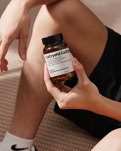 A close-up, high-quality shot of a CoQ10 supplement bottle held in hand, set against a natural, relaxed home background.